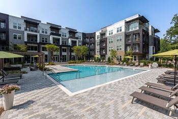 a swimming pool with lounge chairs and umbrellas in front of an apartment building at Century University City, North Carolina